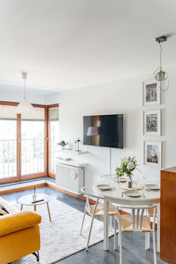 A modern kitchen with a dining area, a TV mounted on the wall, and a balcony with large windows.