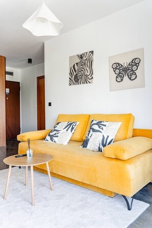 Un salon moderne avec un canapé jaune, une table basse ronde en bois et deux œuvres d’art accrochées au mur.