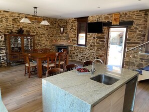 Una habitación de paredes de piedra con una mesa de comedor, sillas, una isla de cocina con fregadero y una chimenea.