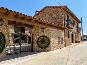 Un edificio de piedra con diseño tradicional, que presenta una gran rueda, una entrada con portón y un balcón.