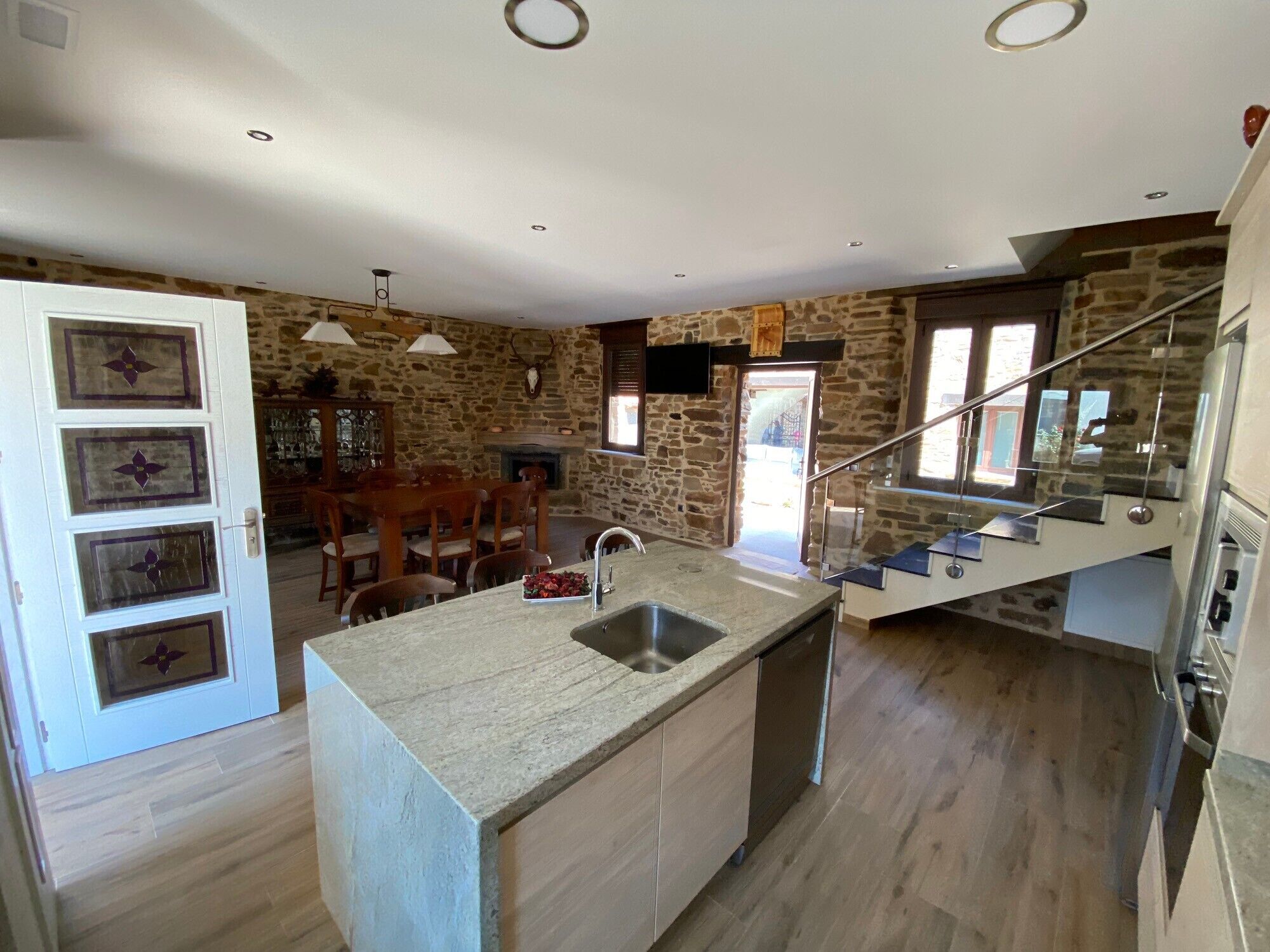 A kitchen with a stone wall, a dining area with wooden furniture, and a staircase.. Casa Amada — Heated Pool, Sauna & Camino de Santiago in Astorga