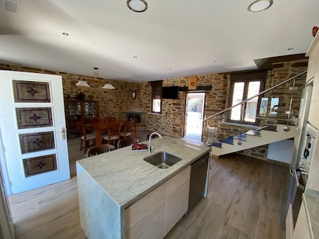 A kitchen with a stone wall, a dining area with wooden furniture, and a staircase.. Casa Amada — Heated Pool, Sauna & Camino de Santiago in Astorga