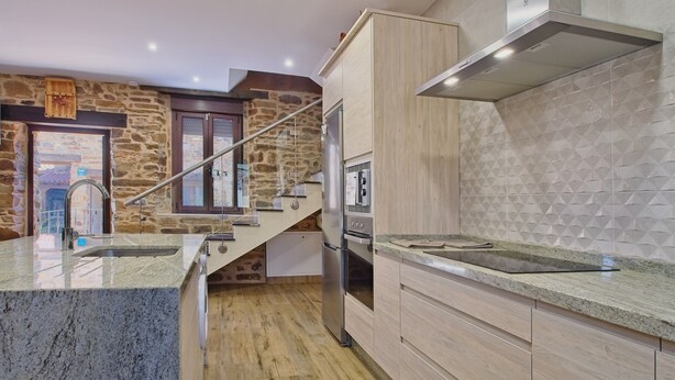 Una cocina moderna con encimeras de granito, un refrigerador de acero inoxidable, armarios de madera y una pared de piedra.