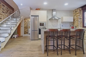 Eine Küche mit einem Edelstahl-Kühlschrank, einem eingebauten Backofen, einer Steinwand und einer Holztreppe.