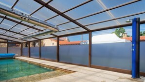 Una piscina con techo de vidrio, una silla azul junto a la piscina y un muro de piedra.