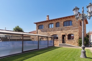 Ein Steinhaus mit überdachter Außenbereich-Sitzgelegenheit und einem gepflegten Rasen.