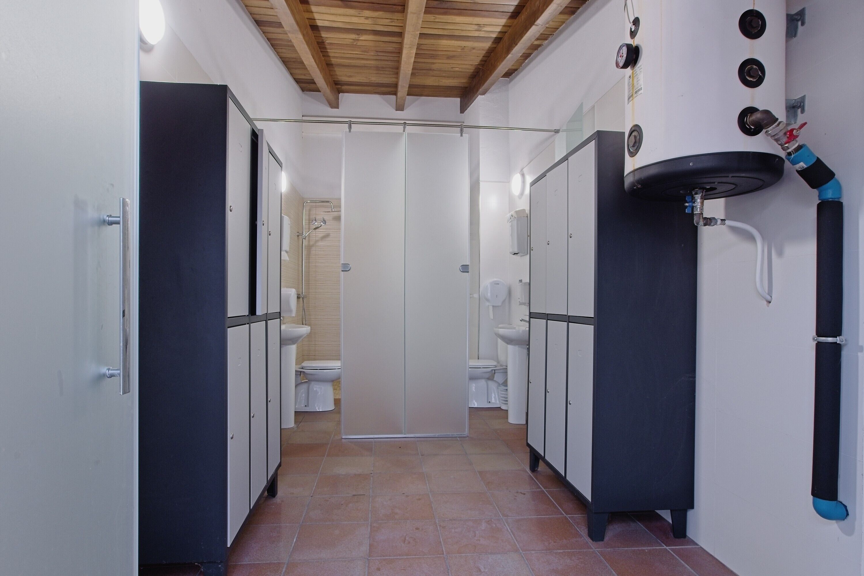 A narrow hallway with a shower area, toilets, and cabinets.