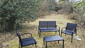 Ein Garten mit einer schwarzen Metallbank und zwei Stühlen.