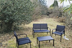 A garden with a black metal bench and two chairs. - Appartement cosy de 55 m2, élégant et rénové et Parking Privé Boulogne sur mer (Boulogne-sur-Mer)
