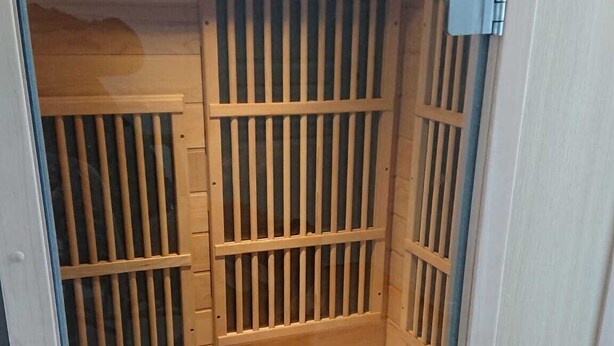 Ein Saunaraum mit Holzlamellen, einer Sitzbank und einer Tür.