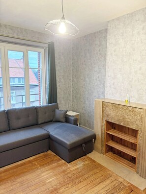 A modern living room with a sectional sofa, a fireplace, a wooden floor, and a large window. - Appartement cosy de 55 m2, élégant et rénové et Parking Privé Boulogne sur mer (Boulogne-sur-Mer)