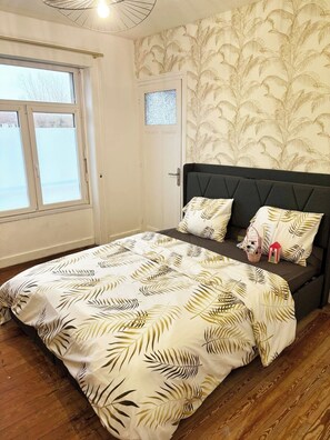 A bedroom with a bed, a window, a door, and patterned wallpaper. - Appartement cosy de 55 m2, élégant et rénové et Parking Privé Boulogne sur mer (Boulogne-sur-Mer)