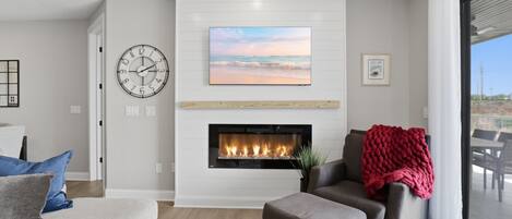 Una sala de estar moderna con chimenea, un reloj y un ventanal grande.