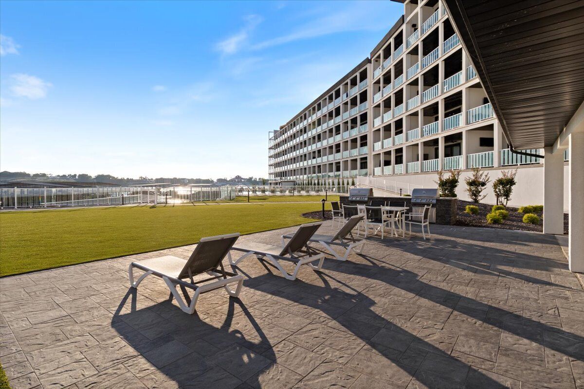 Un hotel con terraza en la azotea que cuenta con sillones de descanso, zona de comedor y vistas a un campo deportivo.