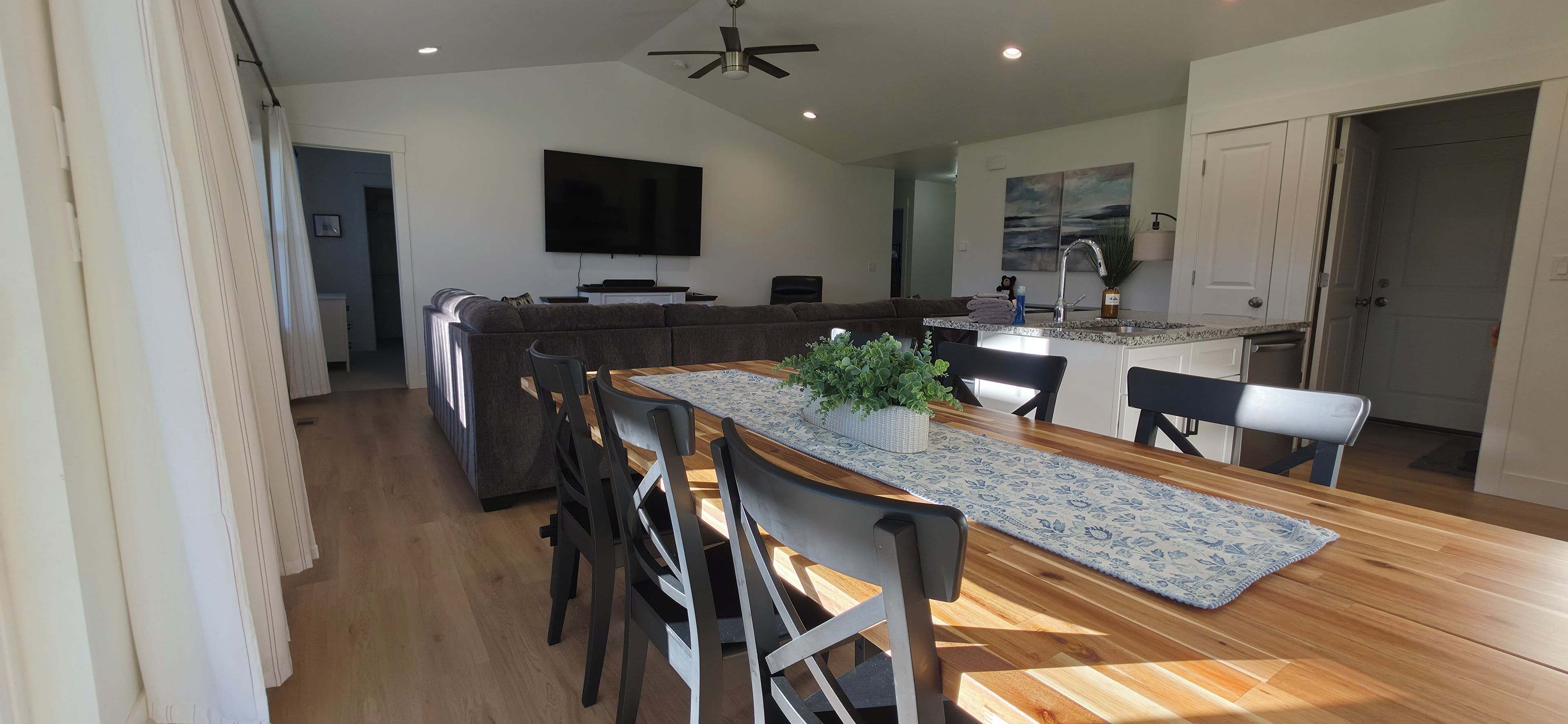 A modern kitchen with a dining area, wooden flooring, and a ceiling fan.