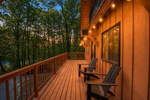 Um deck de madeira com cadeiras e guarda-corpo com vista para uma área arborizada.