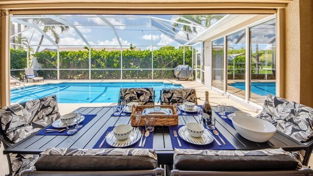 A dining area with a view of a swimming pool, outdoor furniture, and a glass-enclosed patio. - Heated Pool - Spacious - Bike - BBQ- Sound System (Cape Coral)
