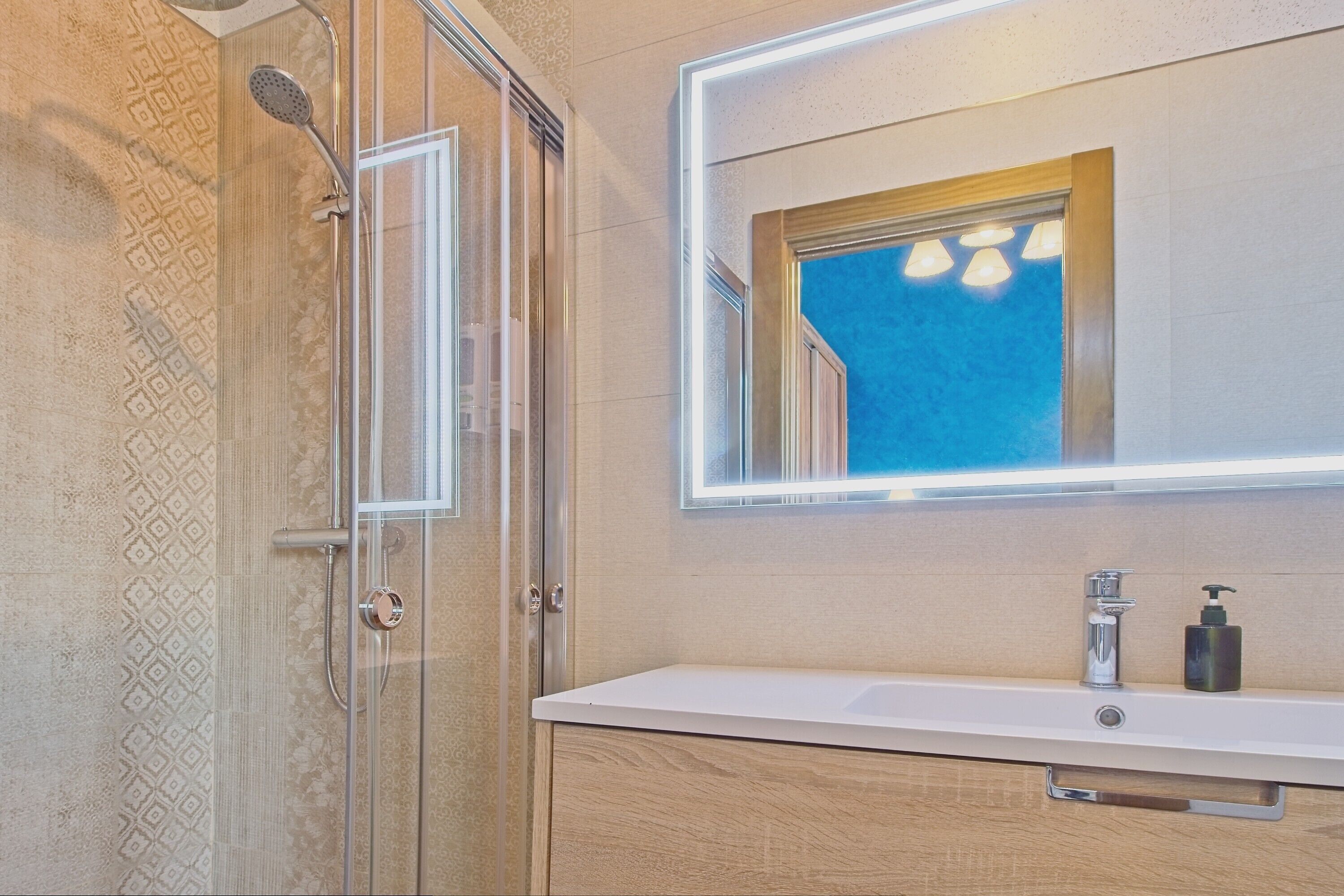 Ein Badezimmer mit Duschkabine aus Glas, einem weißen Waschbecken und einem Spiegel darüber sowie einem Holzkörbchen darunter.