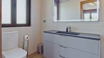 Une salle de bain équipée de toilettes, d’un lavabo, d’un miroir et d’une poubelle.