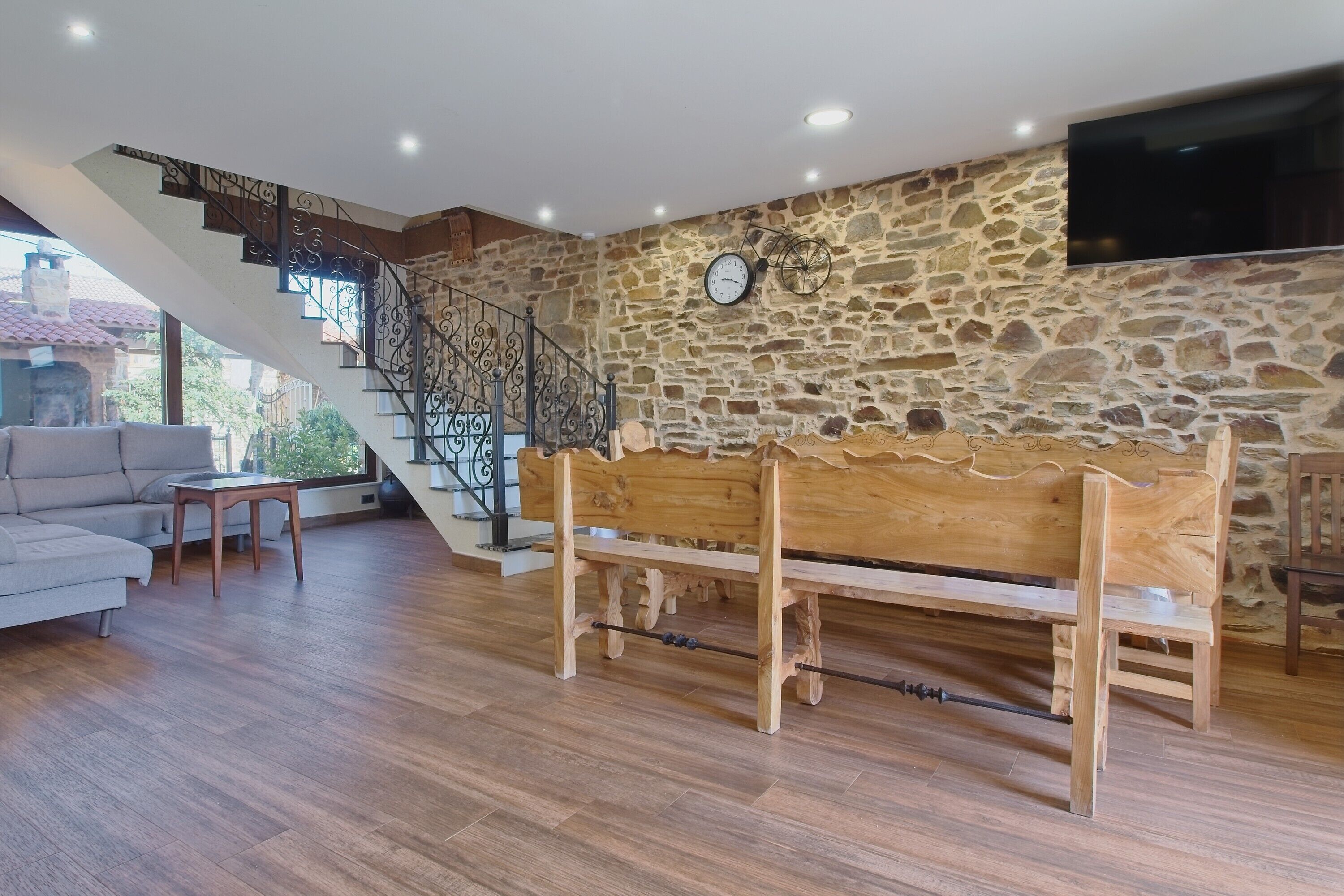 A living room with a wooden bench, a sofa, a staircase with a wrought iron railing, and a stone wall.