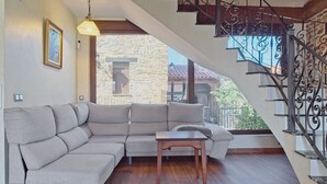 Uma sala de estar com um sofá seccional, uma mesa de centro de madeira e uma escada com corrimãos de metal ornamentados.