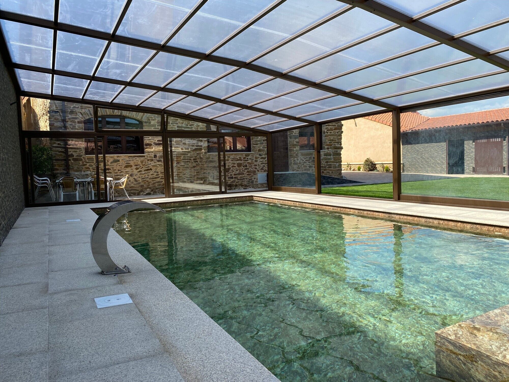 A swimming pool with a glass enclosure, stone walls, and a patio area with chairs.. Casa Enrique — Heated Pool, Sauna, and Camino de Santiago in Astorga