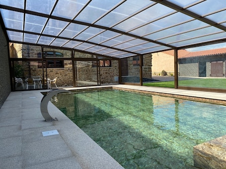 A swimming pool with a glass enclosure, stone walls, and a patio area with chairs.. Casa Enrique — Heated Pool, Sauna, and Camino de Santiago in Astorga