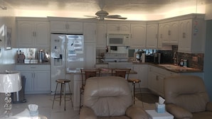 Una cocina con armarios blancos, un refrigerador, un microondas y un comedor con mesa y sillas.