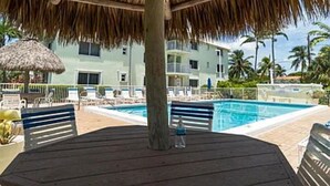 Zona de piscina con techo de paja, una piscina y un edificio al fondo.