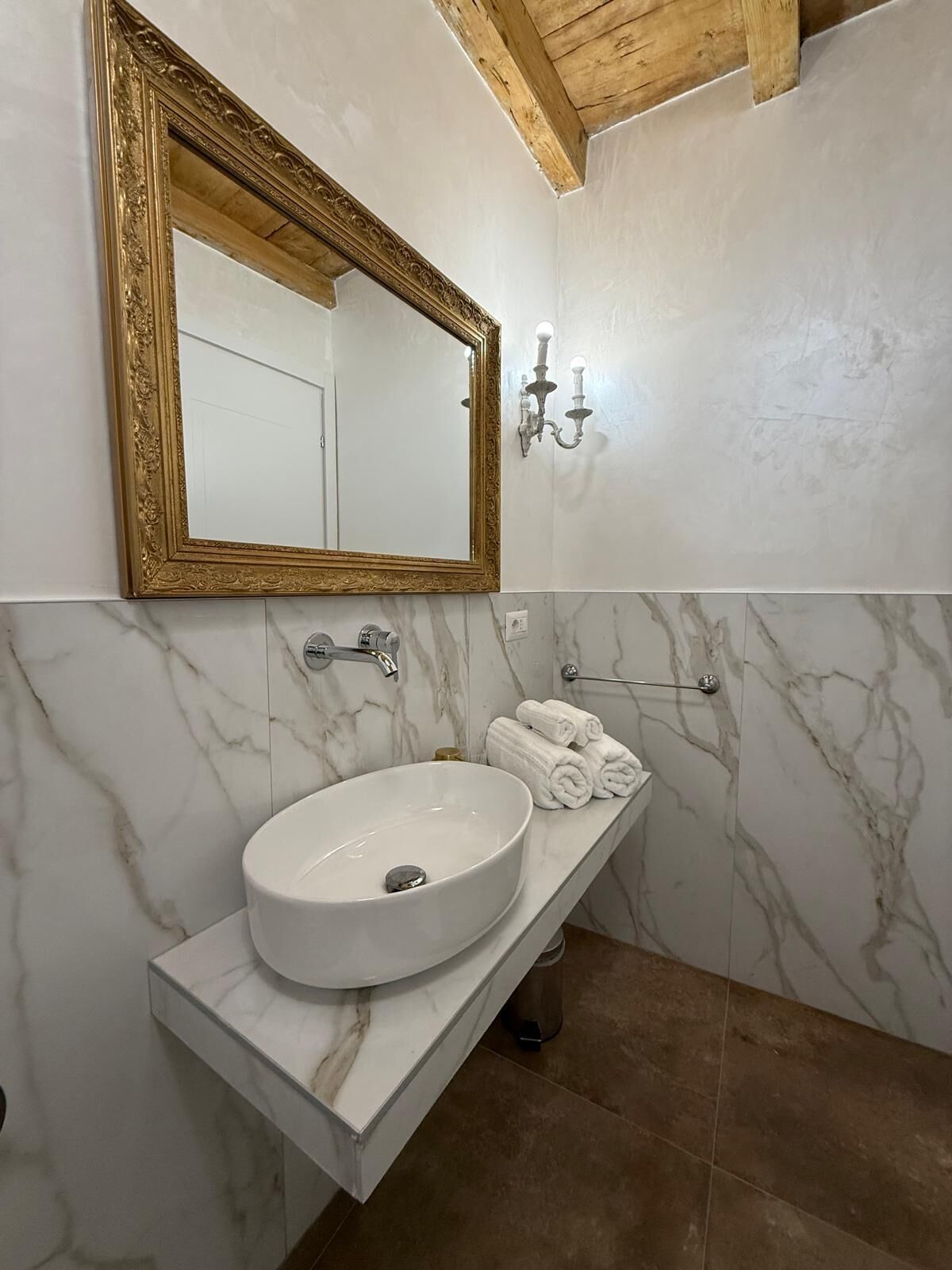 Un baño con lavamanos de mármol, un espejo con marco dorado y un perchero para toallas.