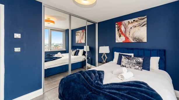 Une chambre moderne avec un grand lit, un miroir et des œuvres d’art accrochées au mur.