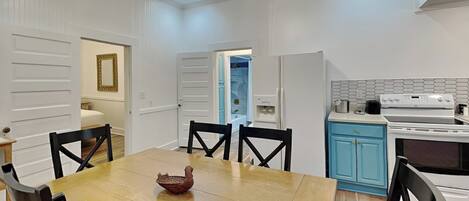 Uma área de refeições com uma mesa e cadeiras de madeira, uma cozinha com eletrodomésticos brancos e um armário azul.