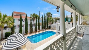 Piscina com deck branco, cercada por palmeiras e um muro branco.