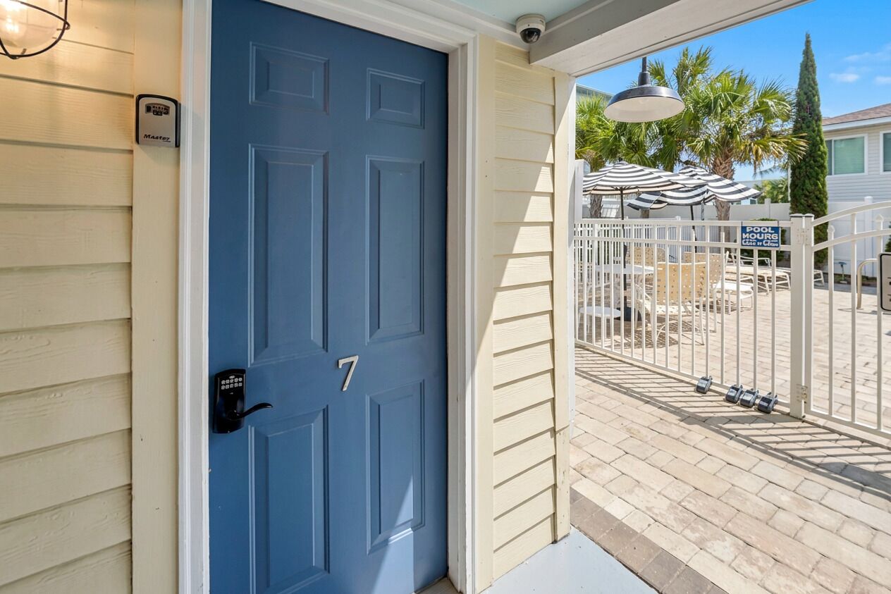 A blue door with the number 7, a mailbox, and a gated pool area with umbrellas.