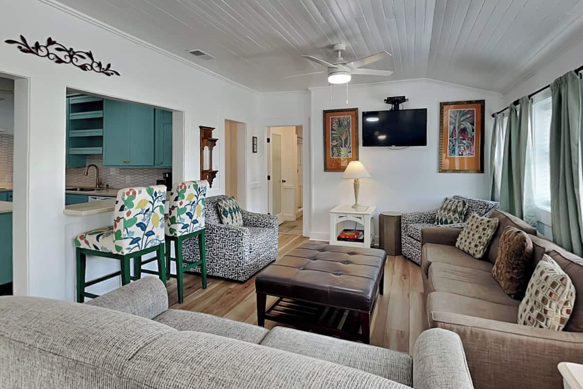 A living room with a sofa, a coffee table, a patterned armchair, a television, and a ceiling fan.