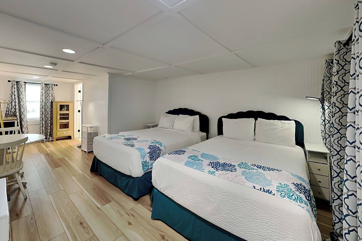 A hotel room with two beds, a desk, a chair, a wardrobe, and a patterned curtain.