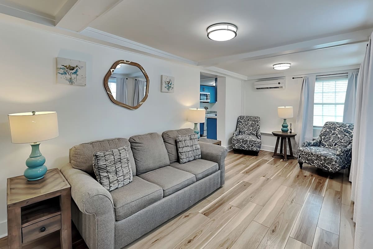 A living room with a sofa, two armchairs, a side table, a mirror, and a ceiling light.