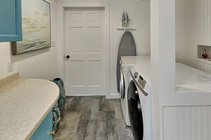 A laundry room with a washing machine, an ironing board, and a door.