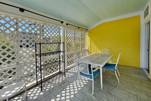 Un porche cubierto con una mesa y sillas, una cerca de celosía blanca y una pared amarilla.