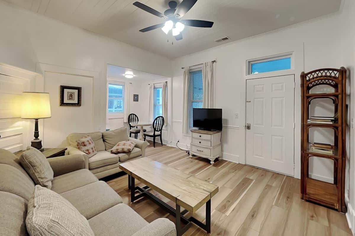 A living room with a sofa, a coffee table, a TV, a ceiling fan, and a wooden bookshelf.