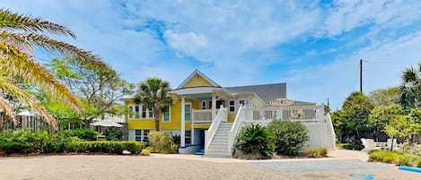 A yellow building with a white staircase, surrounded by greenery and a paved area.
