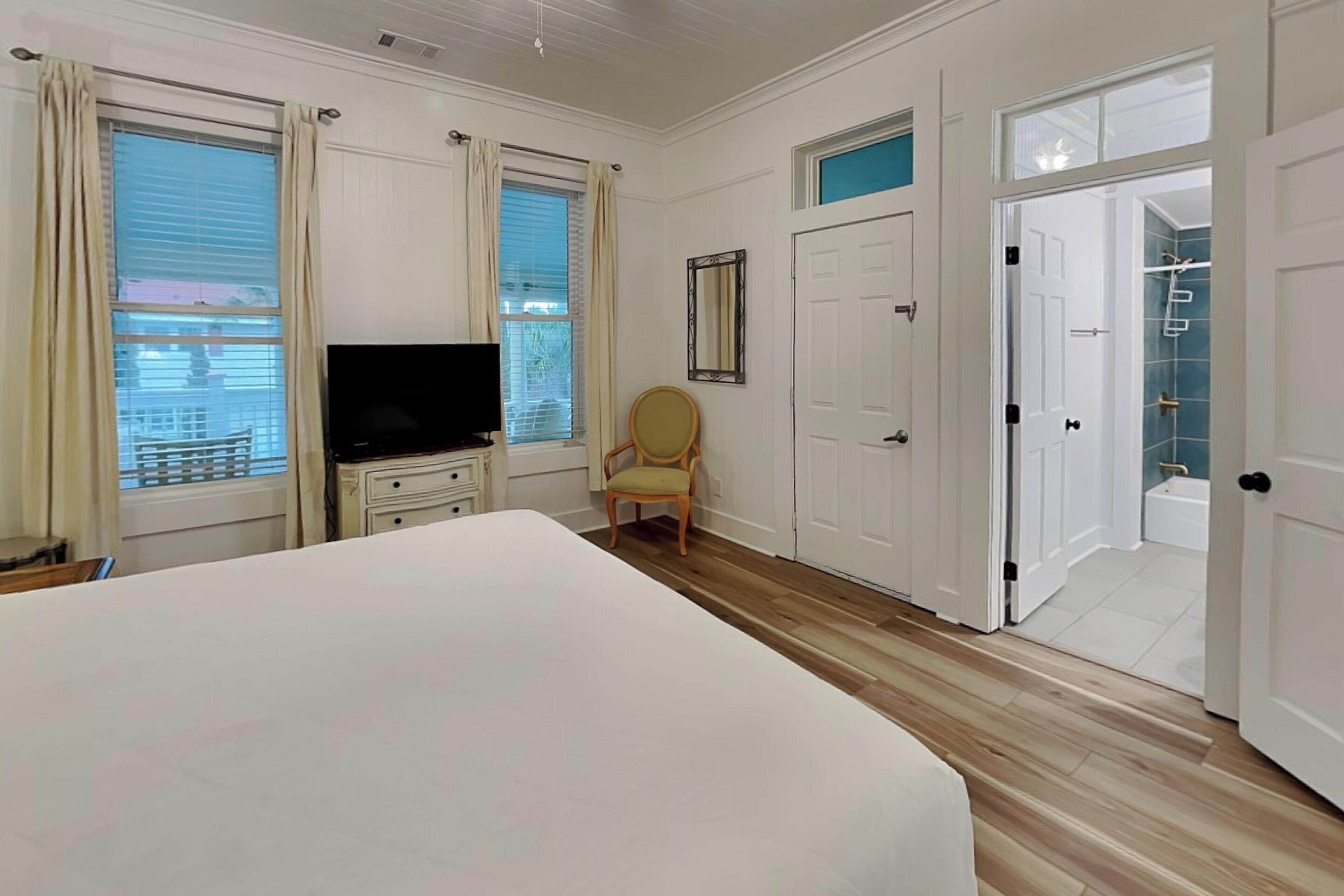 A bedroom with a bed, a TV, a chair, a wardrobe, and a door leading to a bathroom.