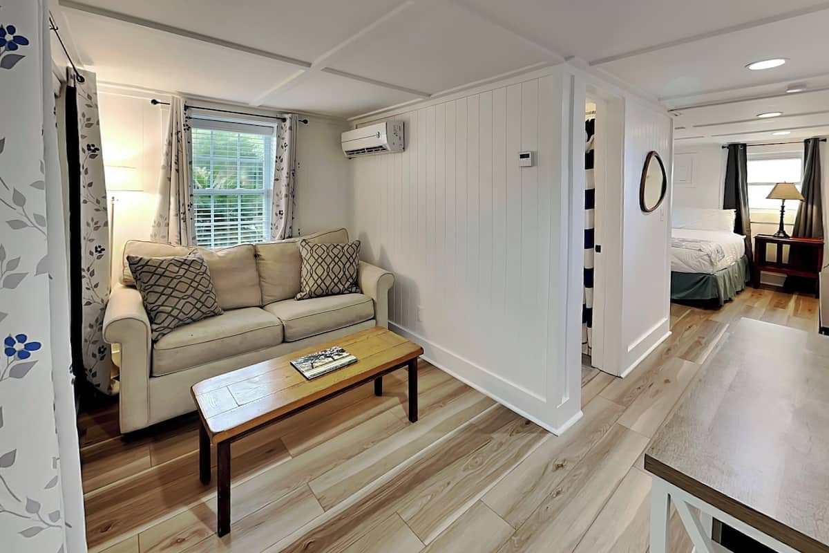 A room with a sofa, a coffee table, a bed, and a small table with a lamp.