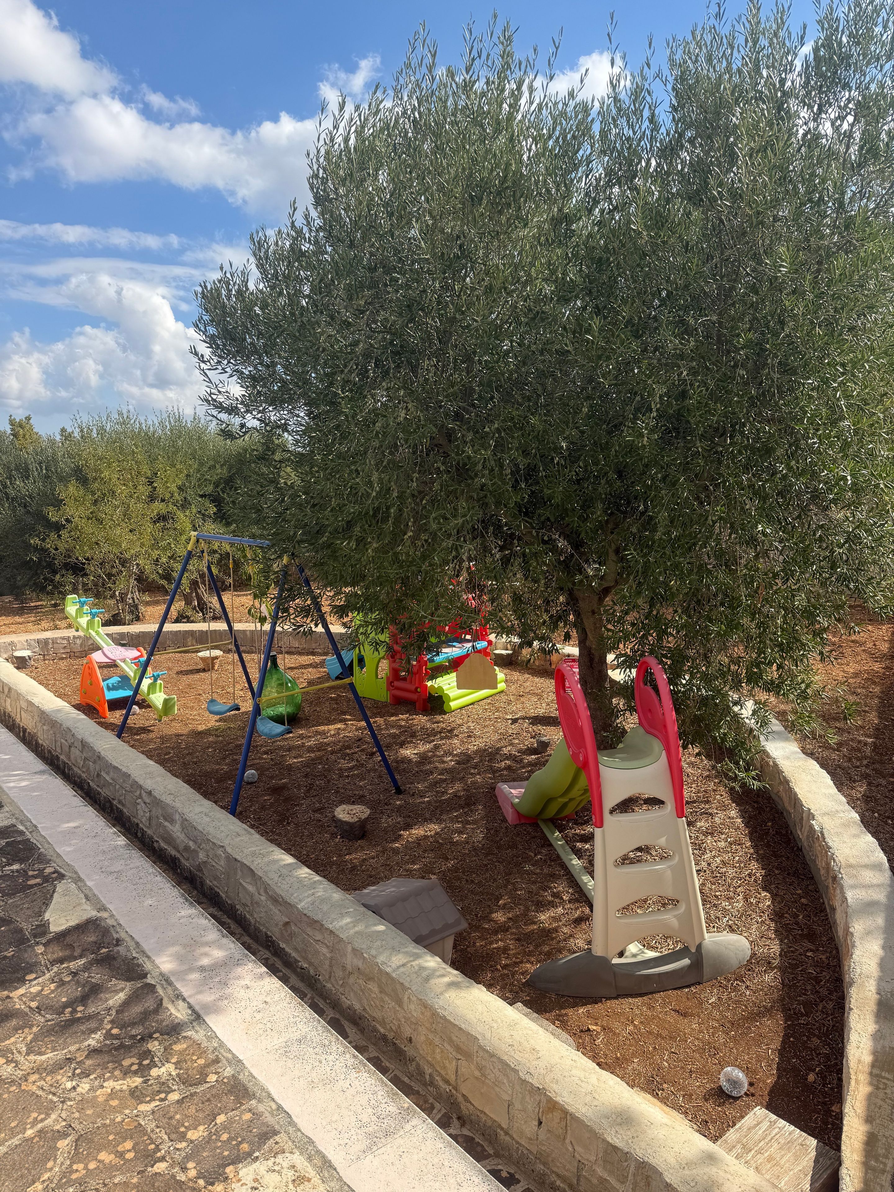 A playground with swings and slides, surrounded by trees and mulch.