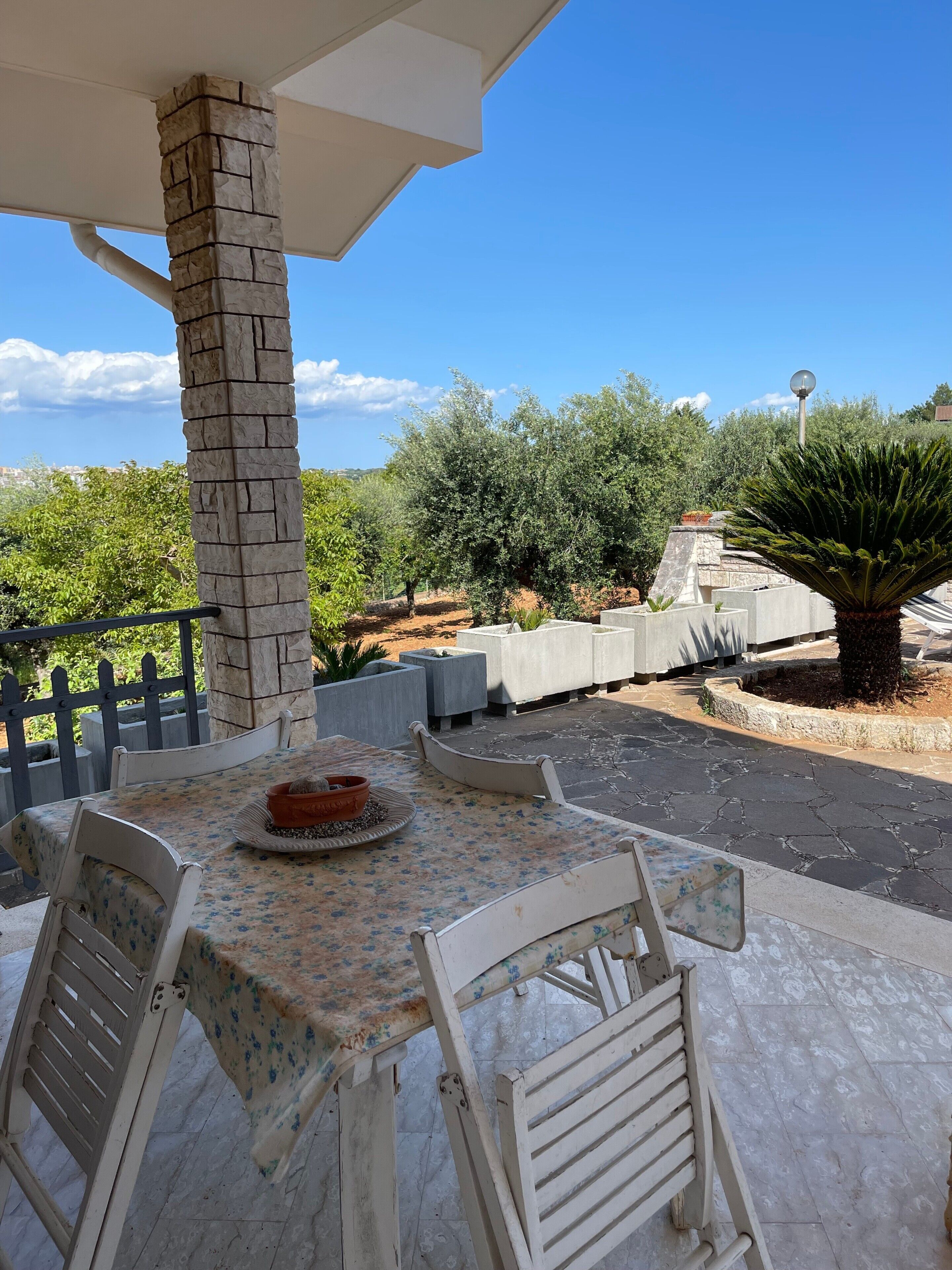 An outdoor patio with a stone pillar, a table with chairs, and a view of the surrounding landscape.