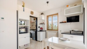 Une cuisine moderne avec des meubles blancs, un four à micro-ondes encastré et une fenêtre donnant sur un paysage pittoresque.
