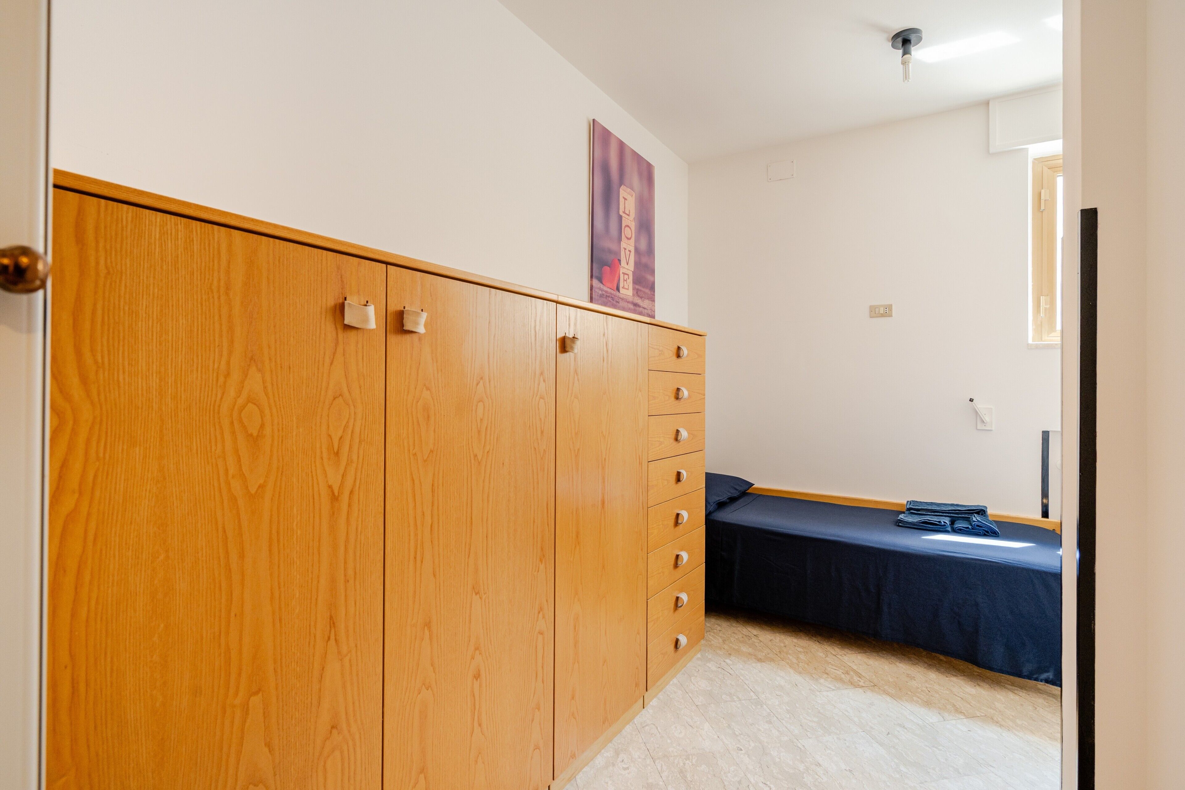 Un dormitorio con un armario de madera, una cama con cubrecama azul y un cartel colgado en la pared.