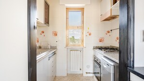 Une cuisine de taille réduite, avec des carreaux blancs, une fenêtre, une cuisinière et un lave-vaisselle.