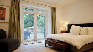 Une chambre avec une grande fenêtre, un lit, une table de chevet, une chaise et un tapis.