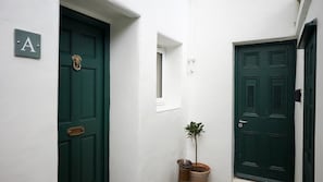 A narrow hallway with two green doors, one marked with a letter 'A', and a small window. - Spacious 1BDR Garden Flat in Charlton (London)